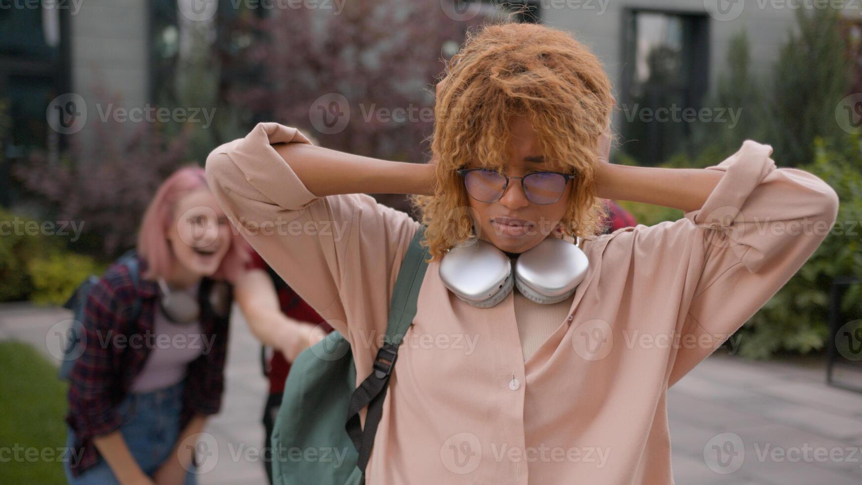 Group of angry students teenagers multiracial classmates mock humiliate bully mockery at college university outdoors discriminate thumbs down African American sad woman student stressed girl problem photo