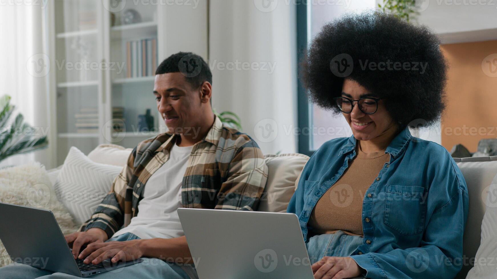 African American couple technology game addict family with two laptops playing online on couch home woman work with laptop man computer working freelancers with computers on sofa separate ignore photo