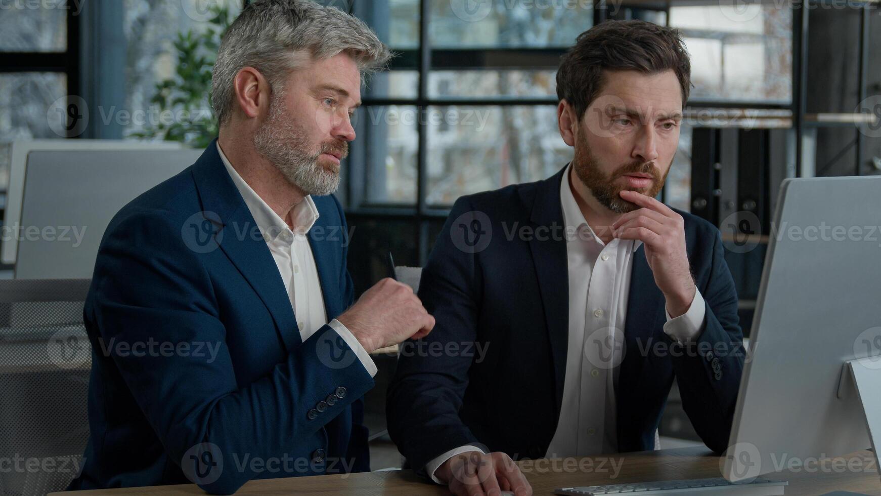 Two serious focused Caucasian men businessmen at meeting in office discussing presentation on computer males business partners coworkers discuss planning commercial online sales client consultation photo