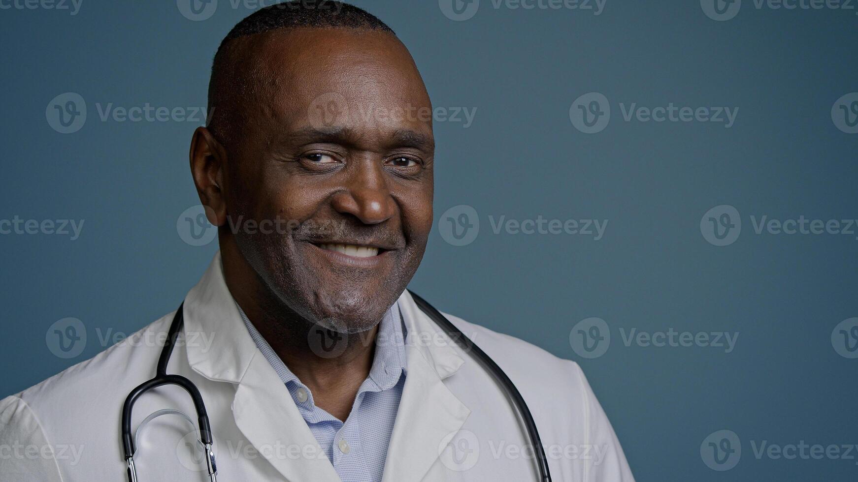 Close-up successful smiling african american man doctor medical worker healthcare employee male portrait cardiologist therapist pediatrician dentist looking camera posing in blue background studio photo