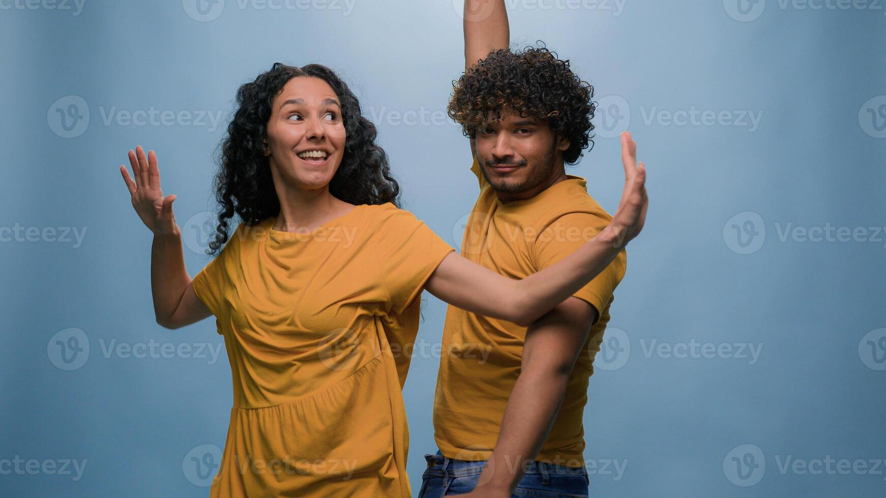 Multiracial diverse couple Indian Arabian man guy Hispanic Caucasian woman girl dancing together to music having fun enjoying funny active moving dance fooling around entertainment at blue background photo