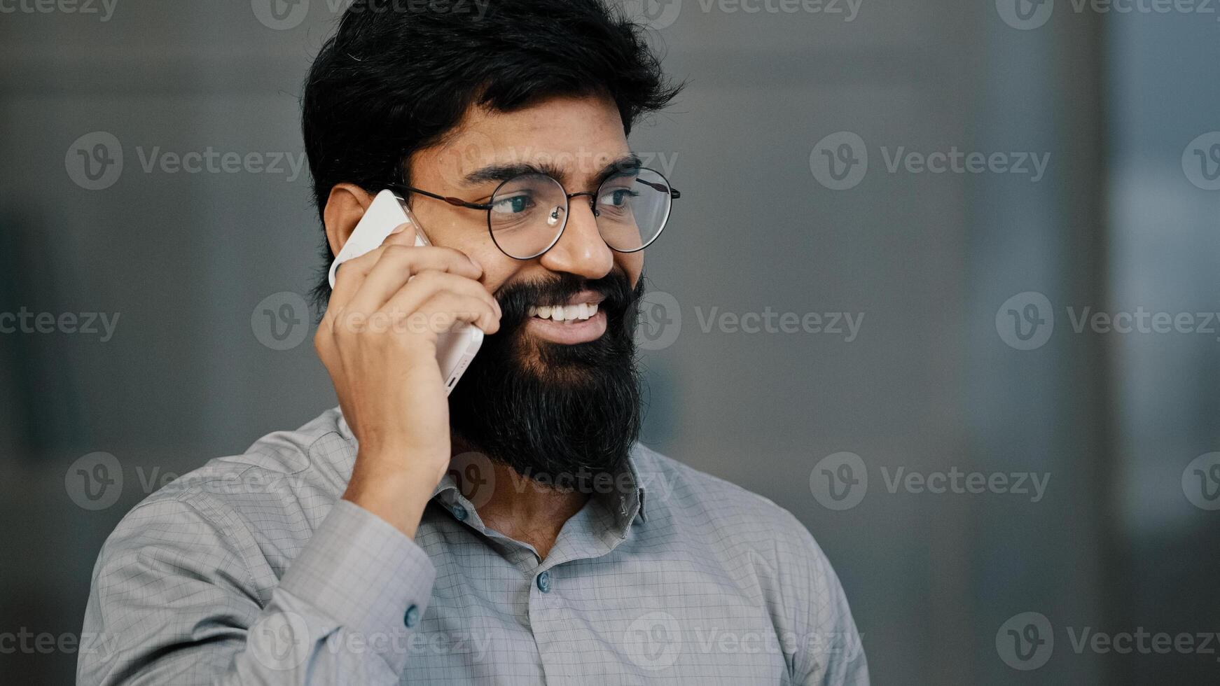 Smiling confident adult millennial man arabian businessman professional worker make business call talk on phone in office happy bearded guy salesman investor hold mobile conversation discuss project photo