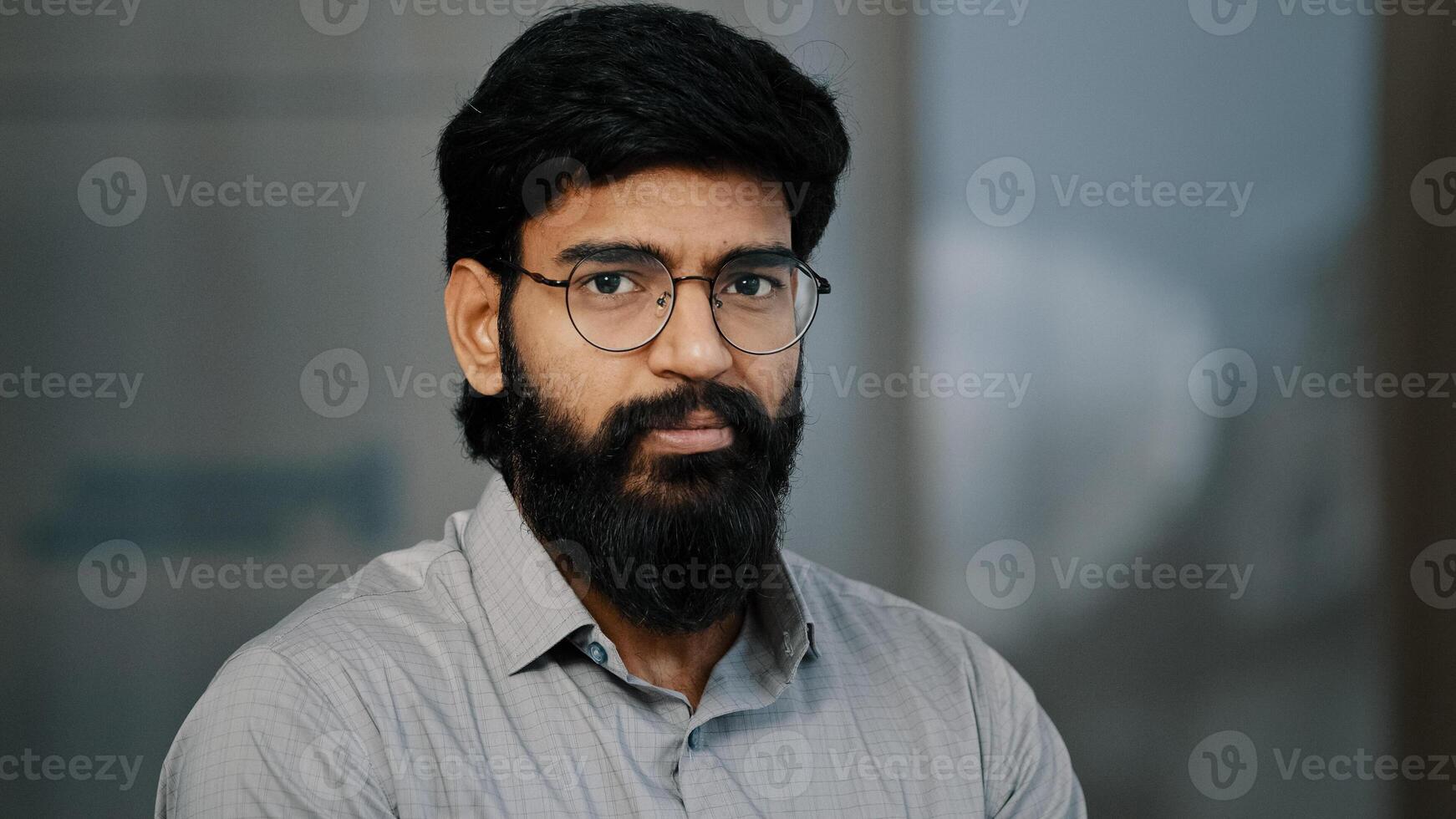 Arab hispanic handsome bearded man confident brunet guy in eyeglasses turn head at camera with positive facial expression indian young intelligent businessman leader worker male founder stand indoors photo