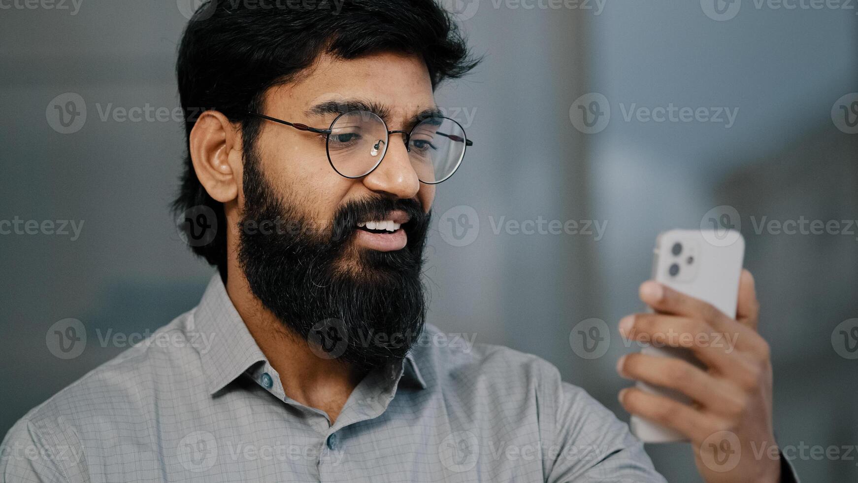 Arabian indian young bearded man businessman handsome entrepreneur hold smartphone talking online communication with business partner virtual meeting enjoy chat using social app greeting remote photo