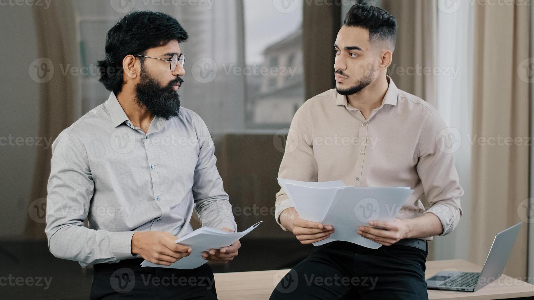 Multiracial diverse co-workers businessmen partners sit on desk hispanic expert consult arabian man colleague hold stack of paper documents discuss financial data insurance contracts teamwork concept photo