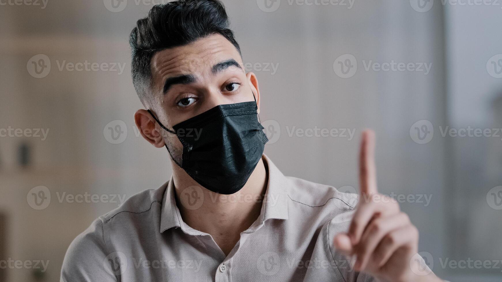 Arabian businessman employee wear medical mask sit at office desk shakes wave index finger warn illnesses infection showing no gesture disagreement sick isolated man avoid offer with negative gesture photo