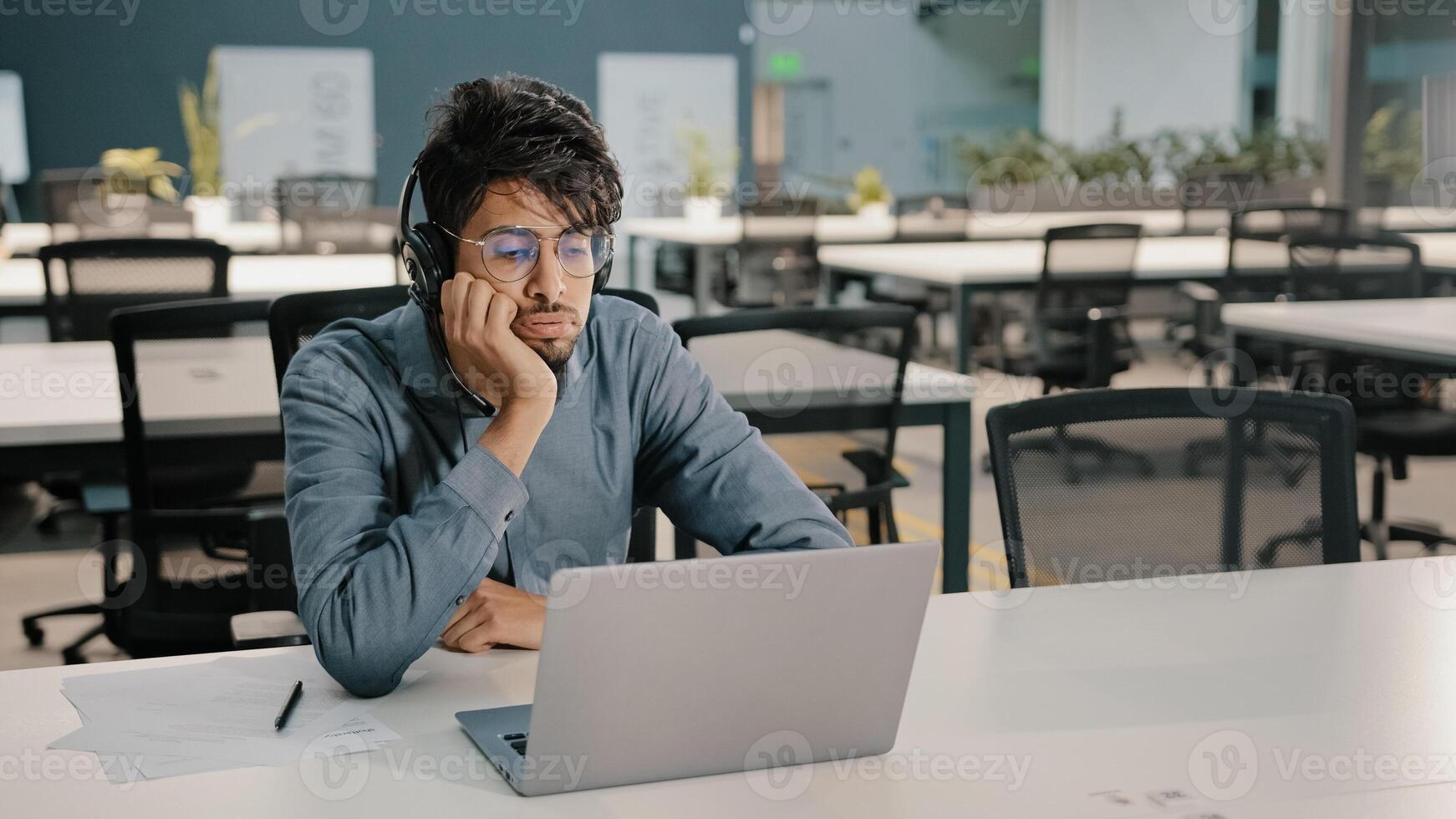 Bored man Arabian man Indian service manager in headphones have displeased look conference webinar learn language improve self-education professional skills studying with difficult task boredom photo