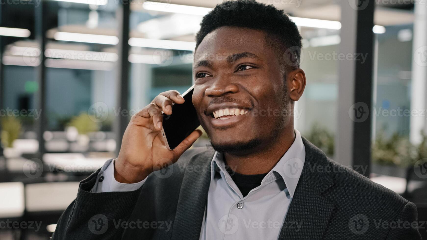African business analyst manager smiling man speaking on cell phone customer consulting communicating emotionally indoor telling story making online order arrange meeting colleague in empty office photo