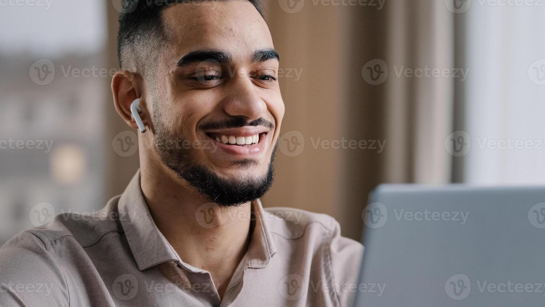 alegre joven Arábica hombre vestir inalámbrico auriculares Mira a ordenador portátil relajarse reloj gracioso comedia película sonriente disfrutar gratis descanso hora leer bueno Noticias Hispano masculino hermoso empresario utilizar moderno computadora foto