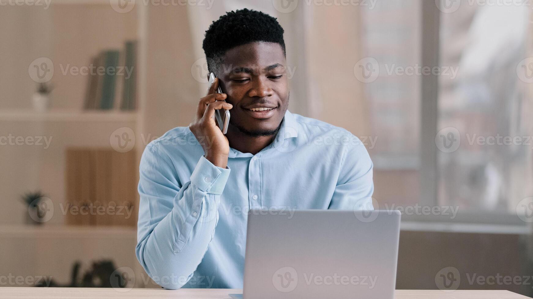 African american man businessman freelancer worker talk chatter on mobile cellphone with client make business call discussion listen news explain information looks at laptop screen use gadget service photo