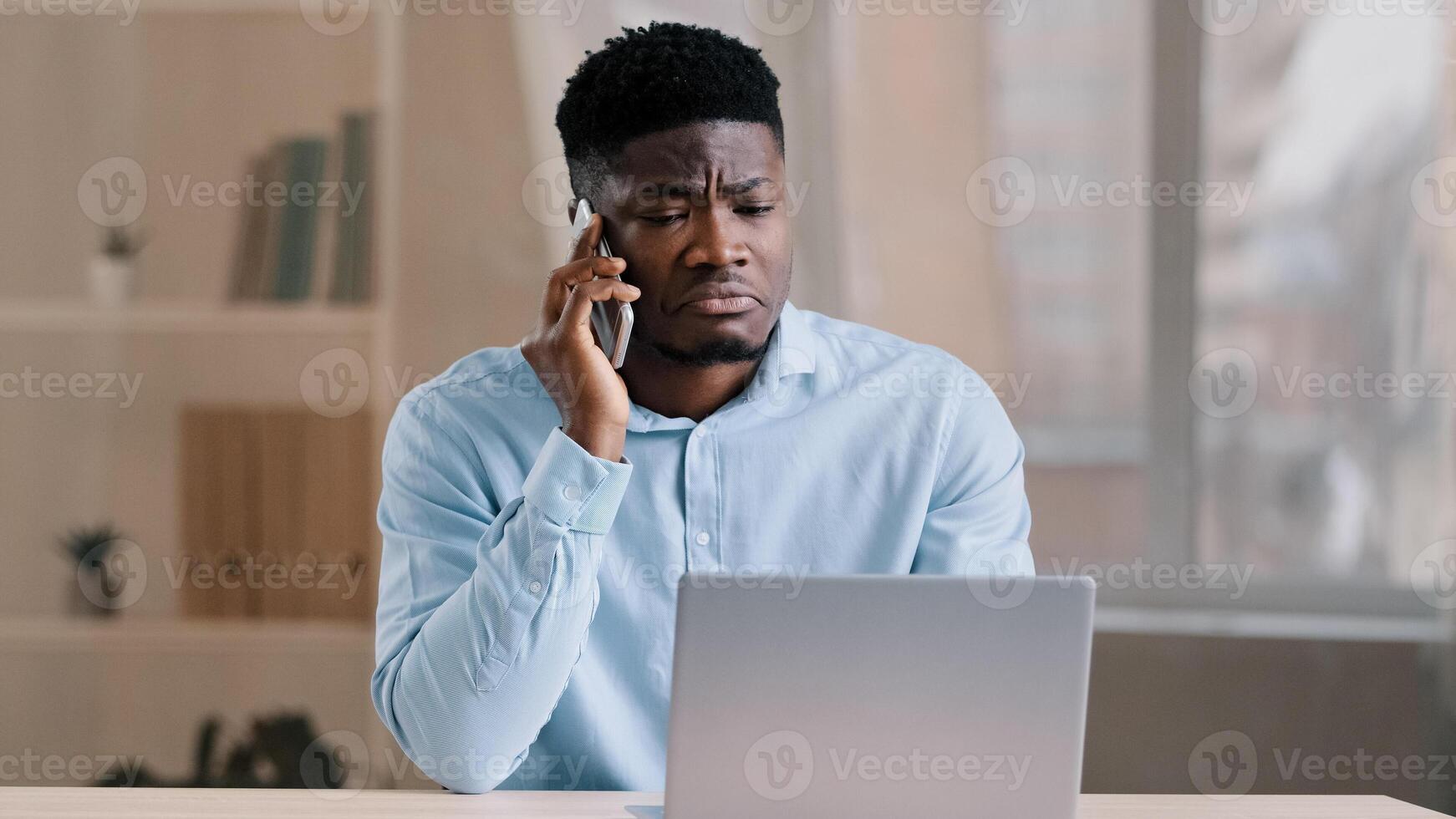 African american man businessman freelancer worker talk chatter on mobile cellphone with client make business call discussion listen news explain information looks at laptop screen use gadget service photo