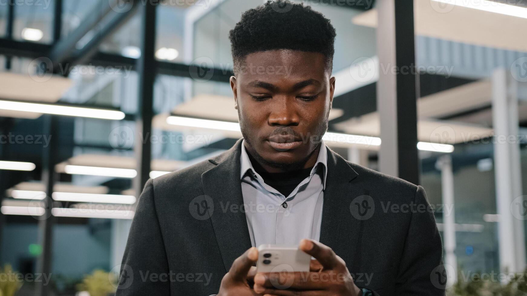 Serious young man african american office worker searching smartphone internet choosing making order chatting online with friends scrolling mobile phone thoughtful male user click at browser account photo