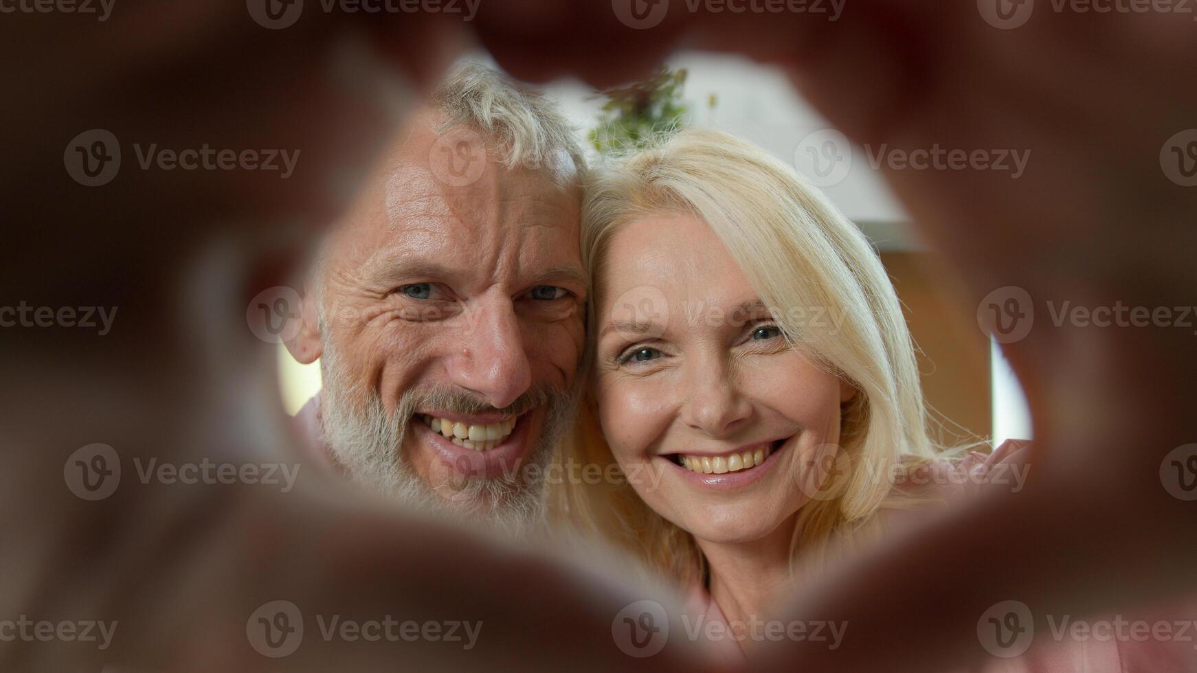 Close-up healthy elderly Caucasian family couple looking through joined fingers make heart shape symbol valentines day celebration romantic relationships eternal love happy long-life marriage concept photo
