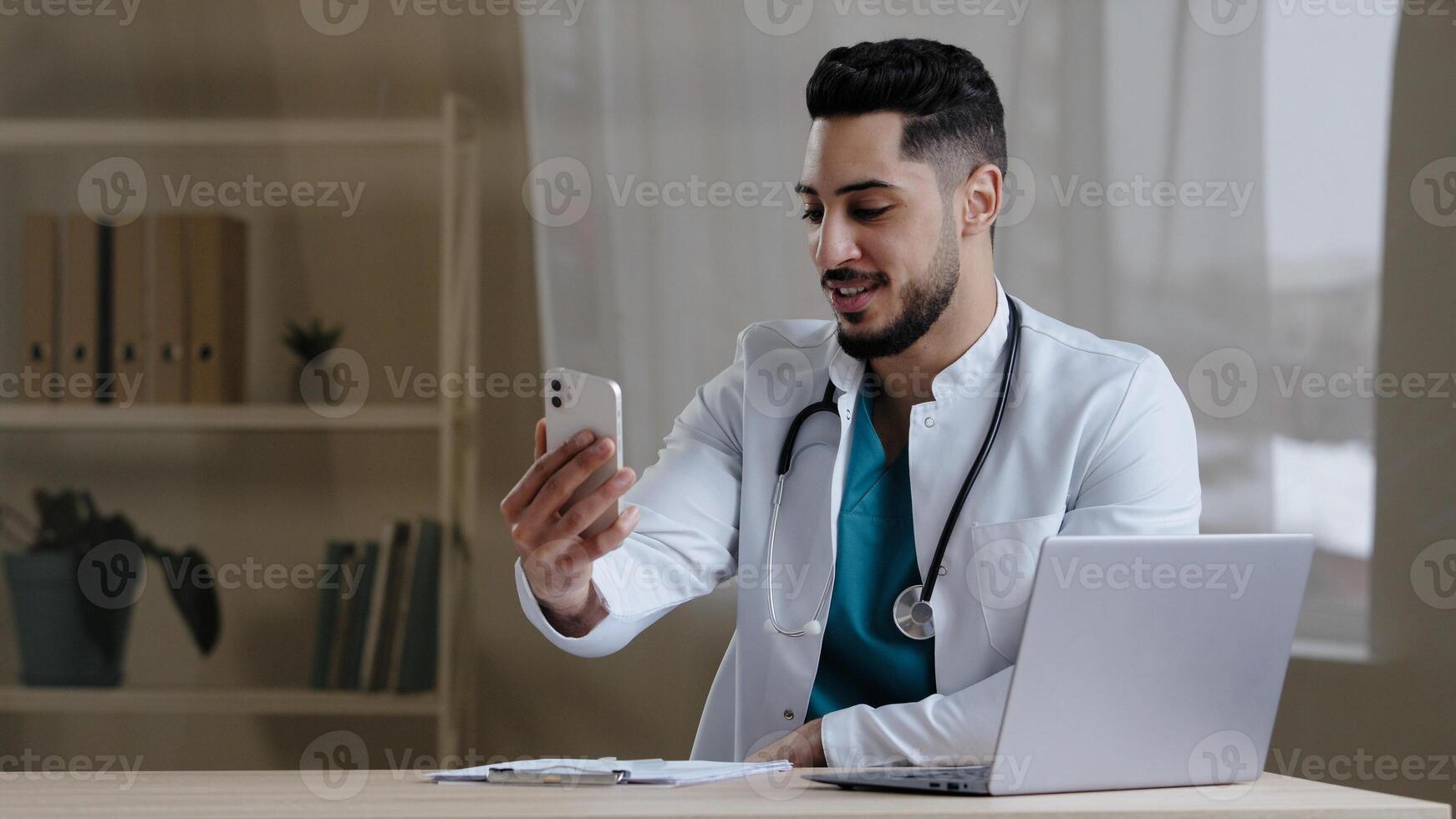 Male doctor general physician hispanic man consulting clients online using via mobile telemedicine application in hospital cabinet remote communicating with medic colleague healthcare services concept photo