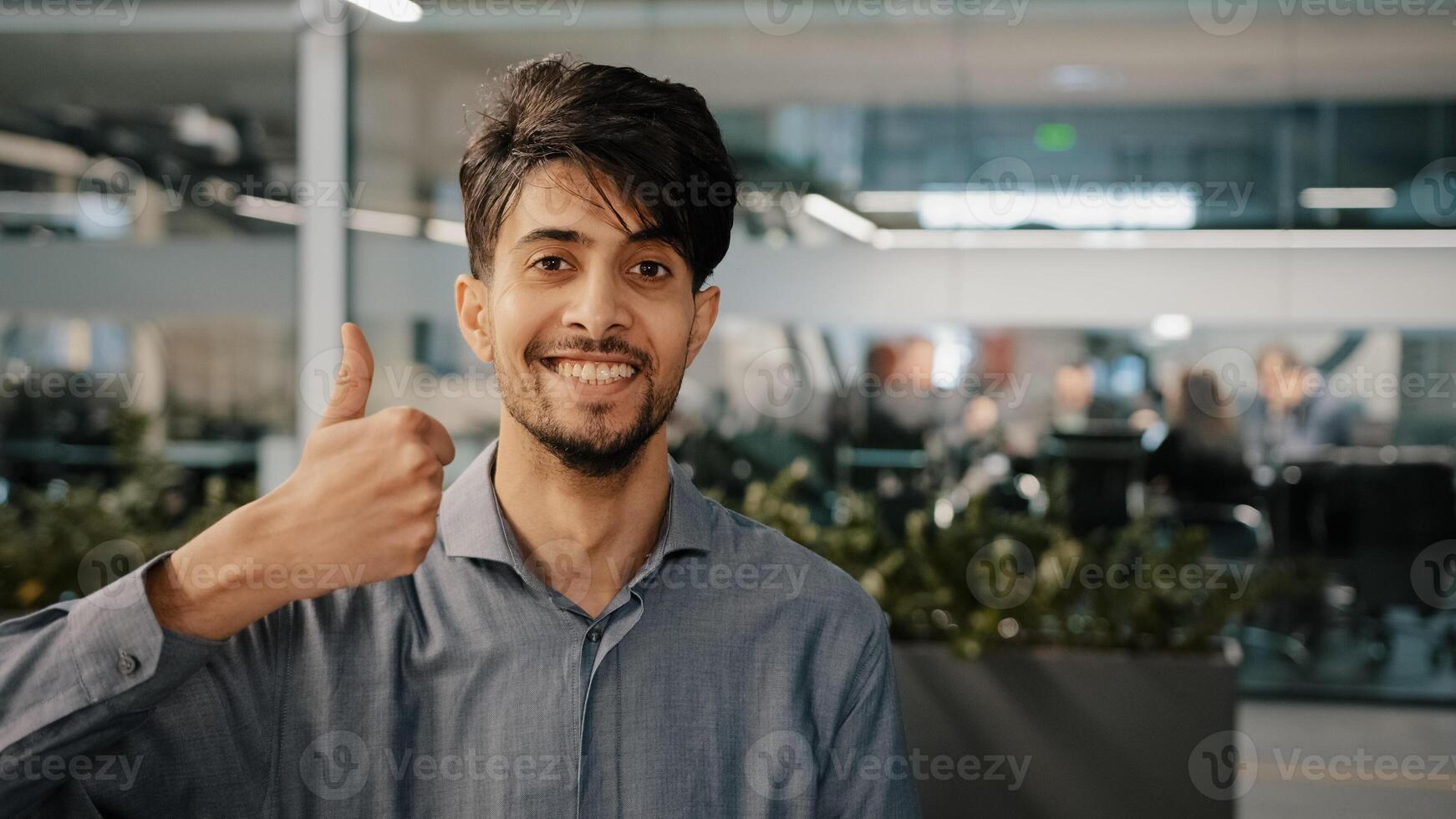 Happy hispanic employee arab man leader winner approve looking at camera showing thumb up agreement sign everything fine success gesture body language in office recommend good choice close-up portrait photo
