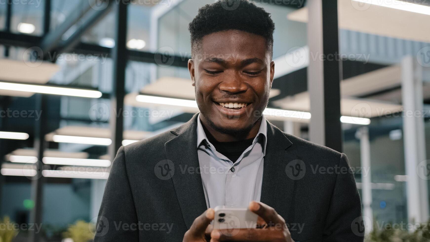 Happy smiling african guy american man businessman boss employee holding modern wireless device texting message on smartphone using social media apps browsing internet playing mobile game at office photo