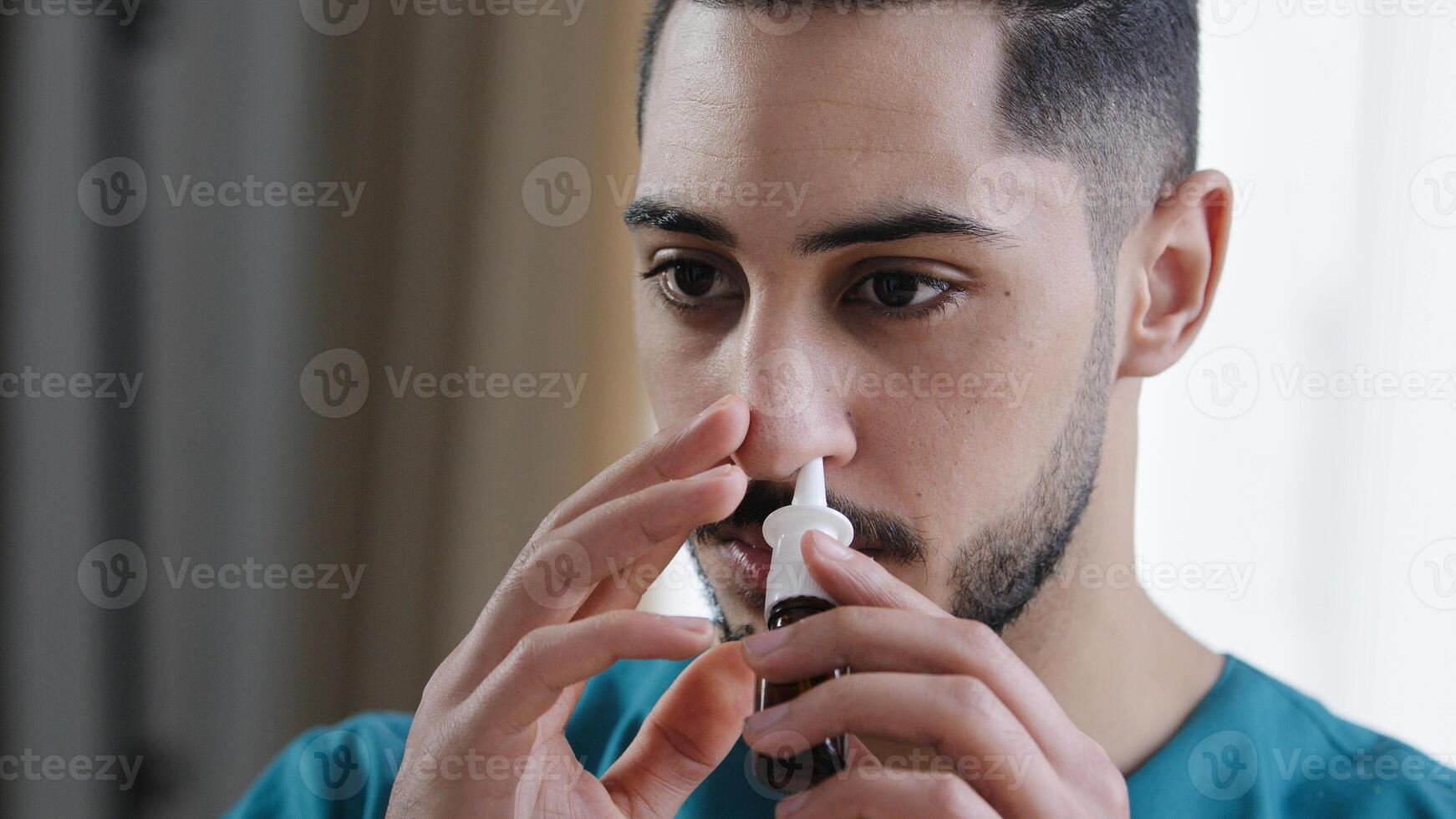 Portrait of sick caucasian man doctor in nurse medical uniform treating runny nose using nasal spray curing snuffle daily therapy from seasonal allergy symptoms at home quarantine health care concept photo