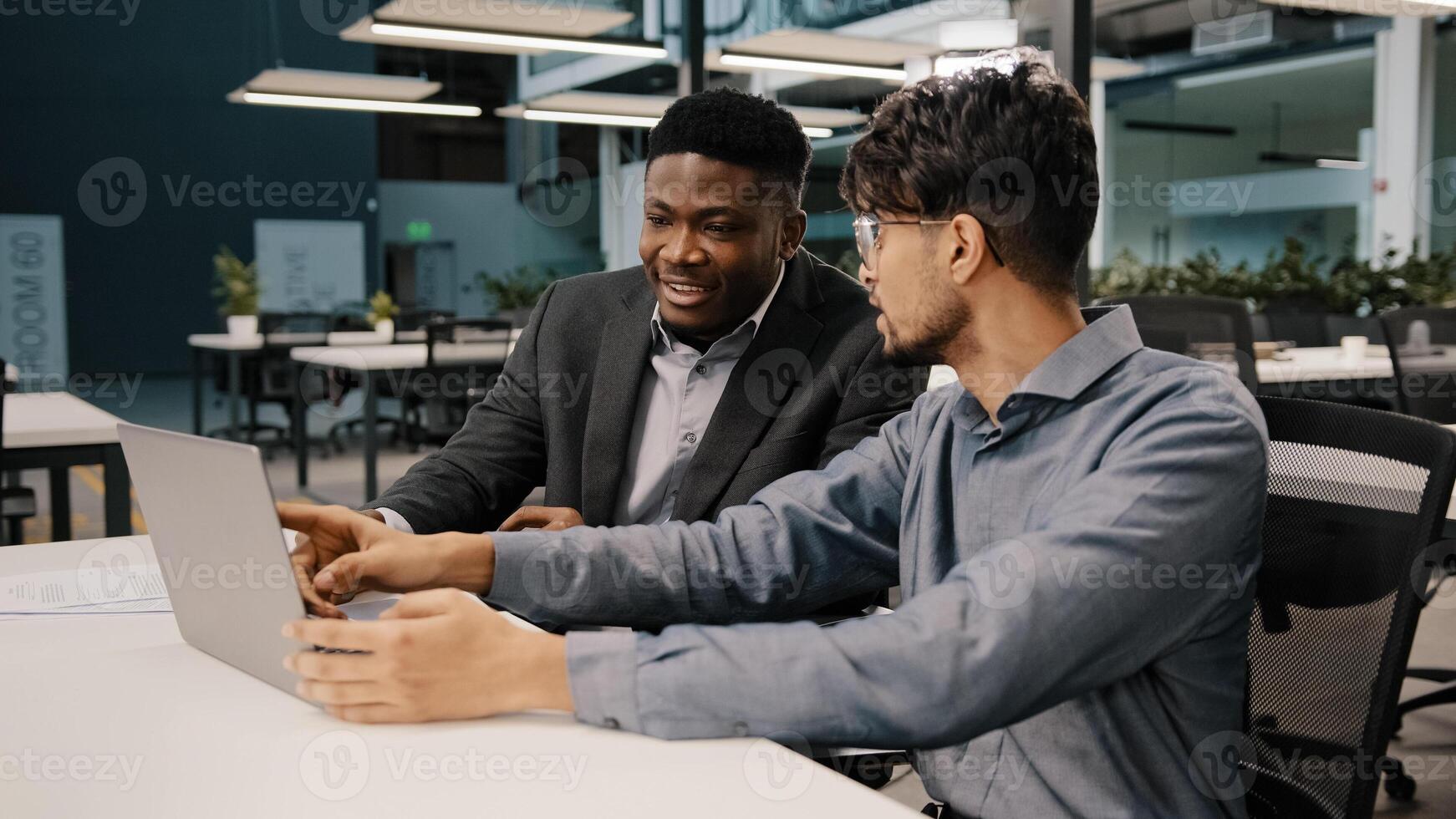 Arabian man financial analyst explain business strategy African entrepreneur pointing on laptop discussing startup reviewing project contract benefits negotiating having teamwork discussion in office photo