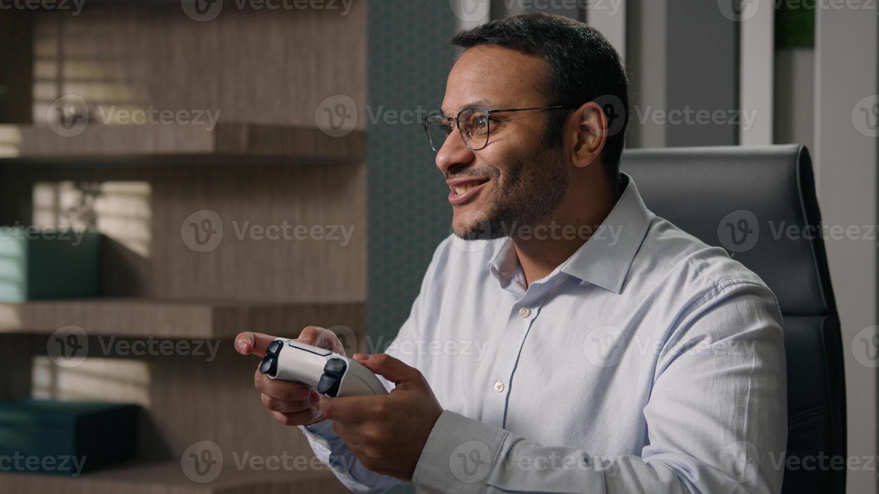Funny lazy worker addicted game Indian man playing console controller play online at workplace in office afraid scared get caught Arabian businessman hide joystick pretend working with computer photo