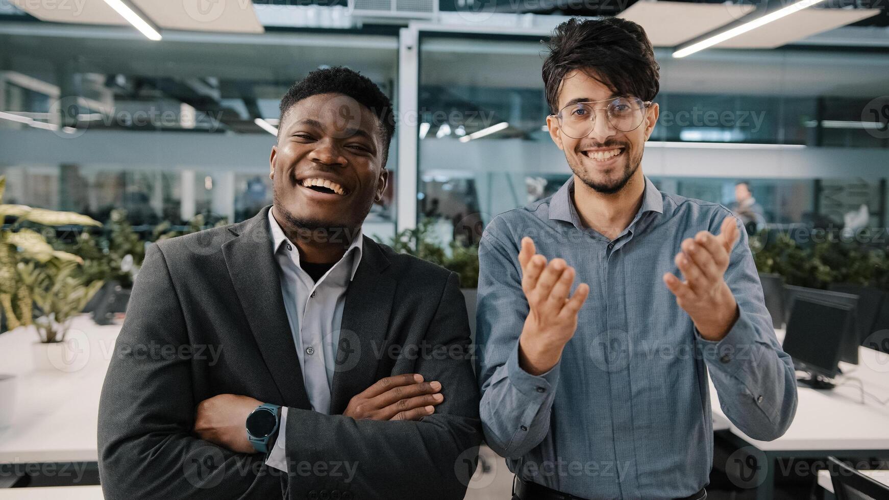 Two cheerful colleagues African man Arabian salesman looking at camera laughing joke funny business situation corporate prank in workspace appreciating good sense of humor rejoice positive atmosphere photo