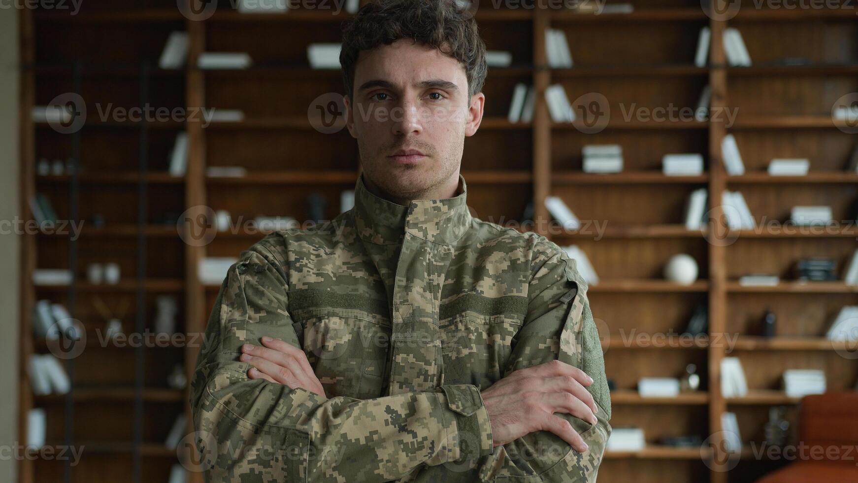 Confident strong young Caucasian male officer man guy in camouflage Ukraine uniform military army soldier patriot crossing arms cross hands serious sad veteran looking camera indoor office room clinic photo
