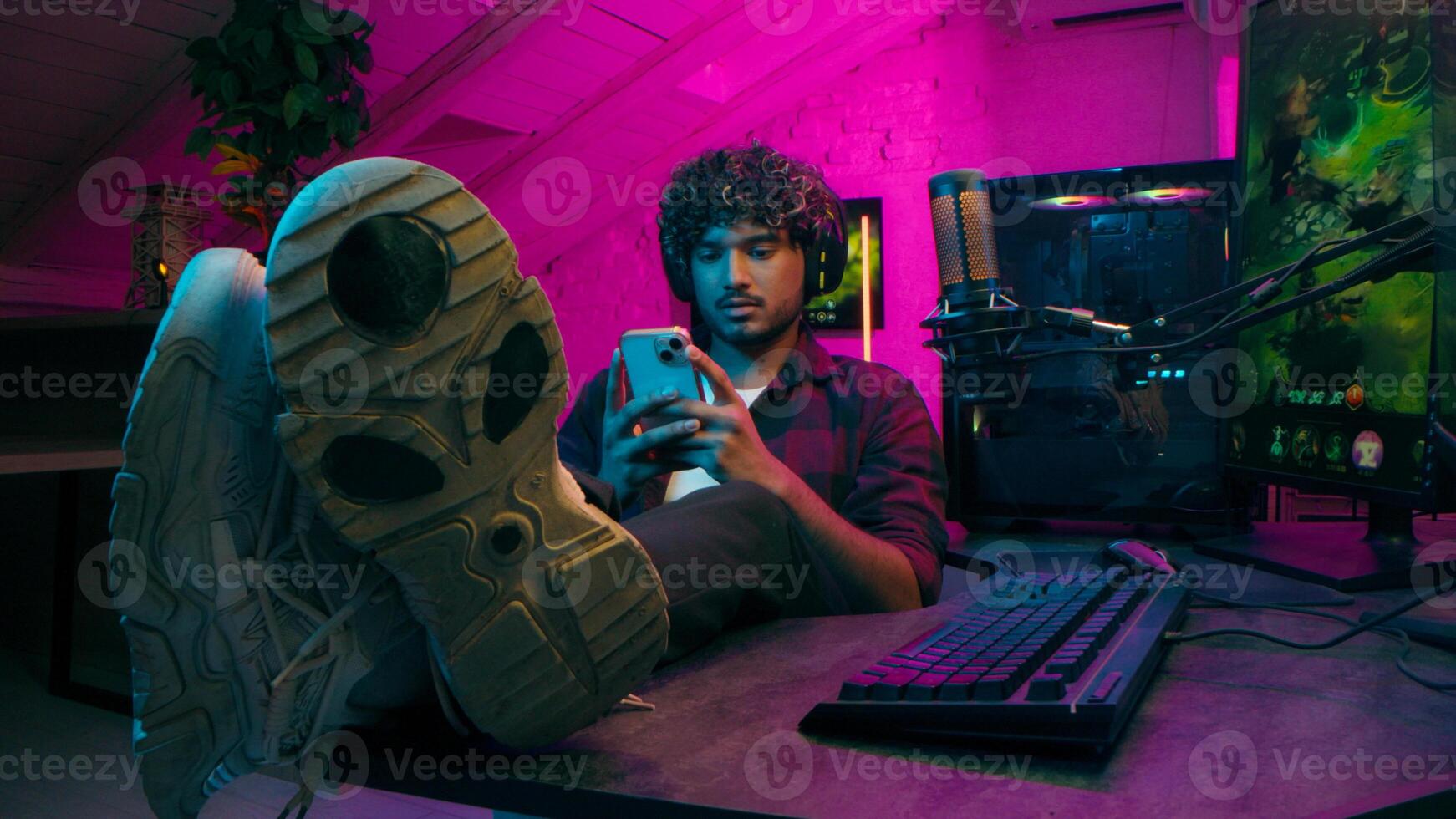 Indian American man gamer gambler computer game technology mobile phone smartphone pc addiction pause network keyboard excited male mouse put feet table gadgets guy stuck connection cyber electronic photo