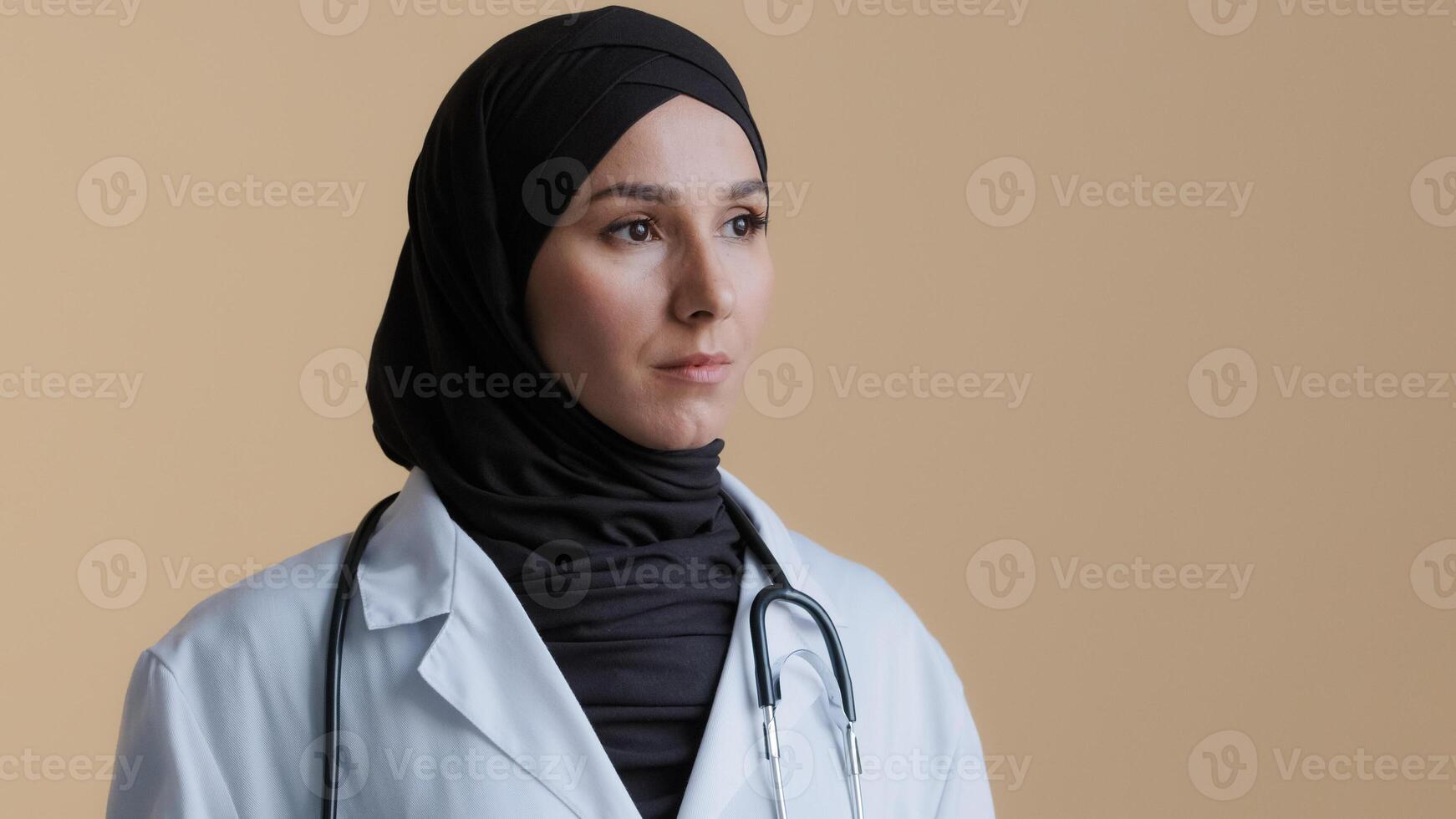 Portrait of pensive upset muslim arabian young woman doctor islamic gynecologist scientist physician in hijab headscarf thoughtful female medical pharmacist dreaming girl stand over beige background photo