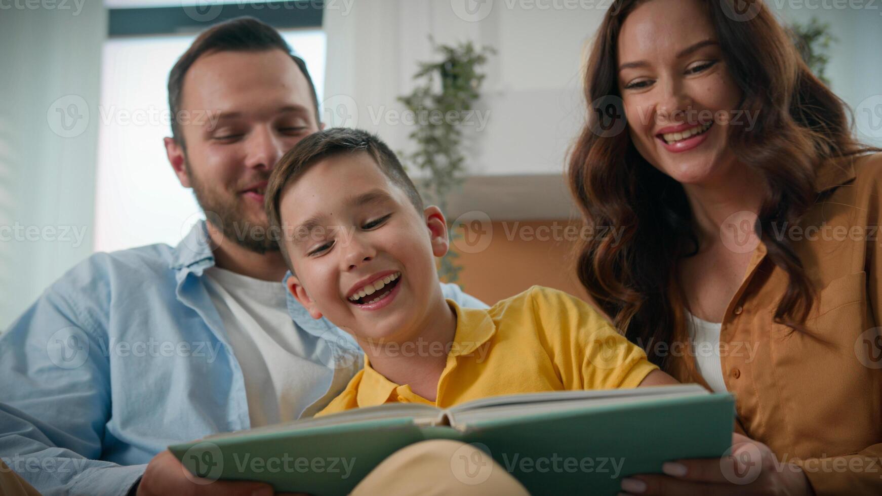 Mother father son reading book together in cozy living room loving parents read fairy tale boy child funny happy caucasian family relaxing laughing enjoying weekend hobby development education support photo