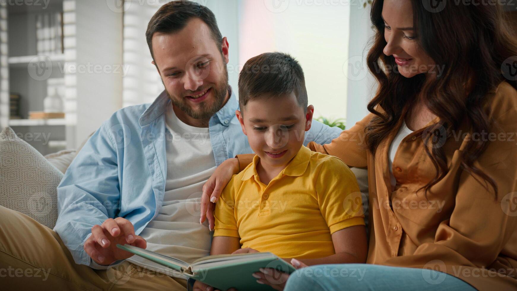 Caucasian mother father son reading book in cozy living room on couch spending weekend together caring loving parents storytelling boy child enjoying read fairytale relax happy family relationships photo