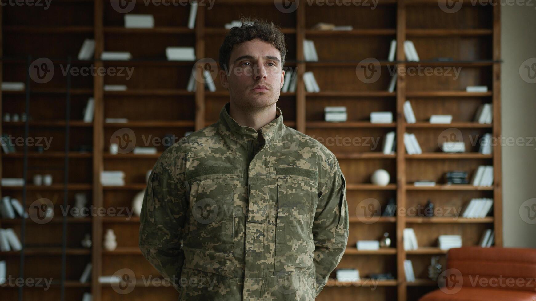 Calm confident Caucasian serious man male guy in military combat uniform army soldier serving in armed forces veteran warrior officer posing with hands behind back looking distance at home office room photo
