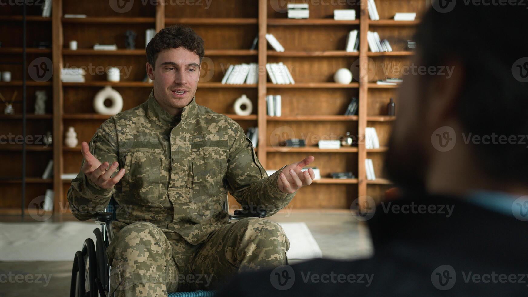 Caucasian client male patient in camouflage uniform man with disability military army soldier guy in wheelchair talking gesturing sharing thoughts with psychologist counseling mental health at office photo