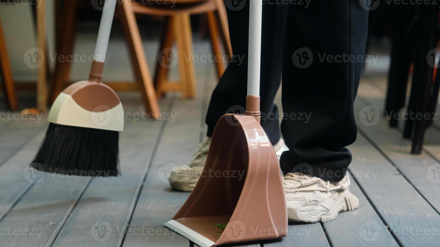 Indian Arabian man cafe worker in apron entrepreneur male businessman guy waiter cleaner working small business owner sweeping leaves using broom cleaning preparing restaurant for visitors city street photo