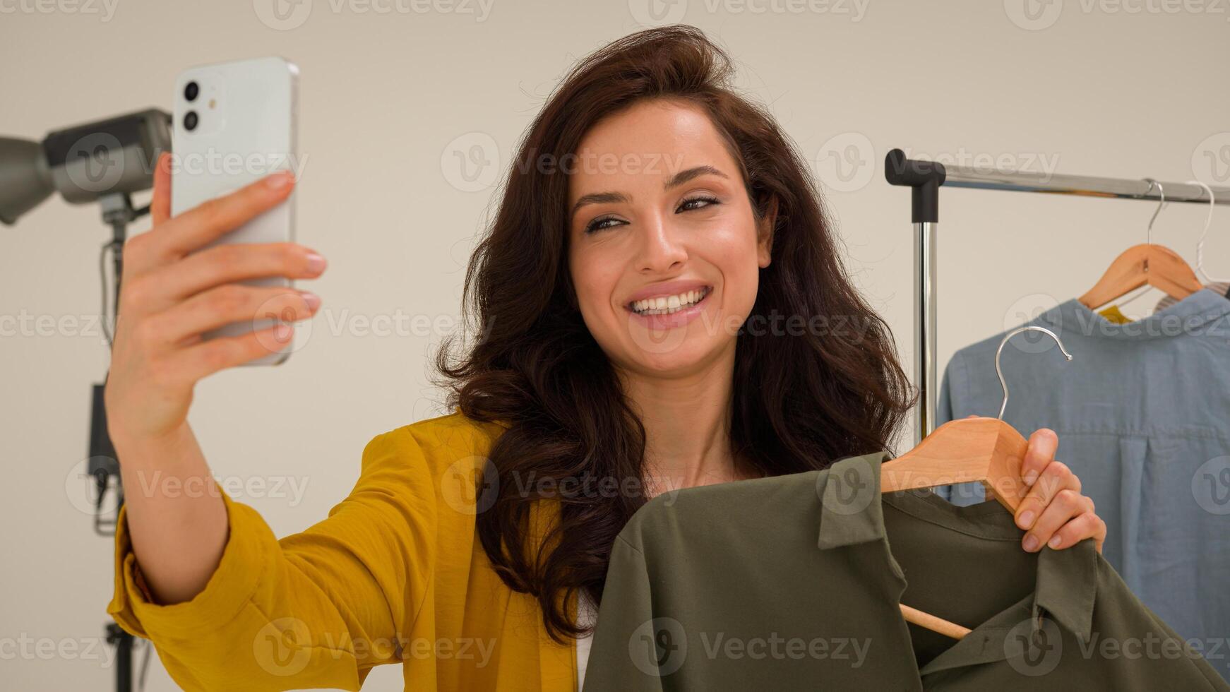 Smiling Caucasian woman glad girl trendy vlogger famous streamer recording stylish on mobile phone device in studio happy female talking explain fashion blogger showing wardrobe broadcast blog photo