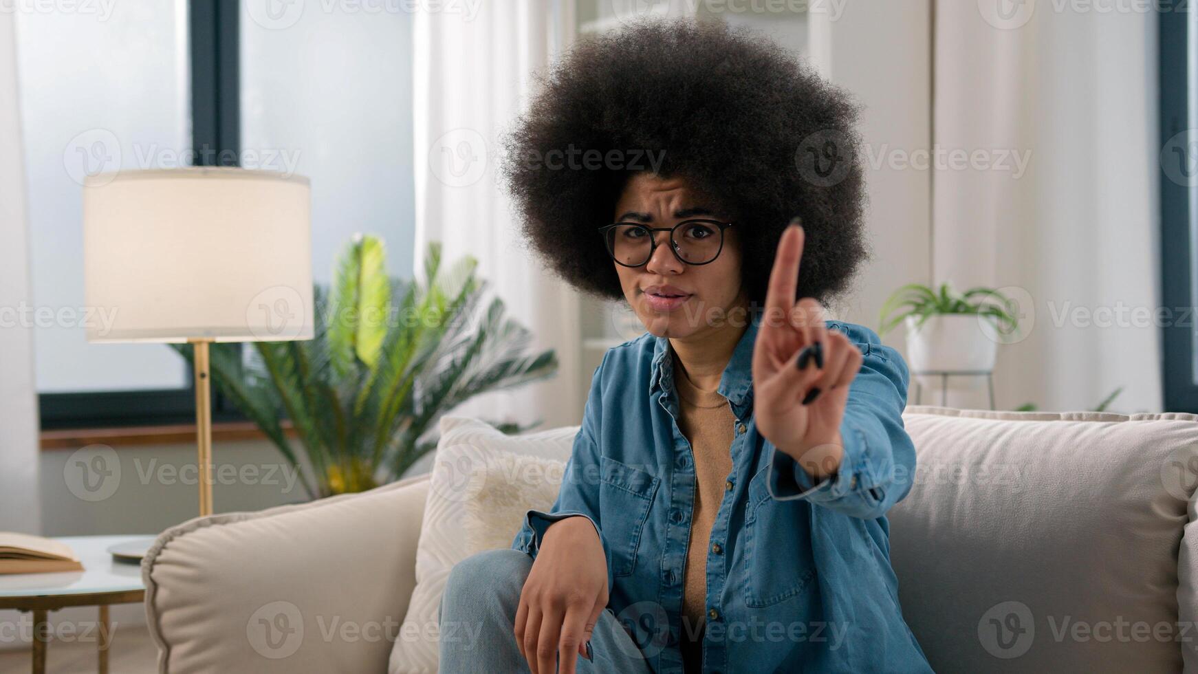 Serious confident ethnic girl African American woman at home sitting on couch sofa waving finger no not never gesture forbid showing negative answer attitude reject deny refuse reaction stop hand sign photo