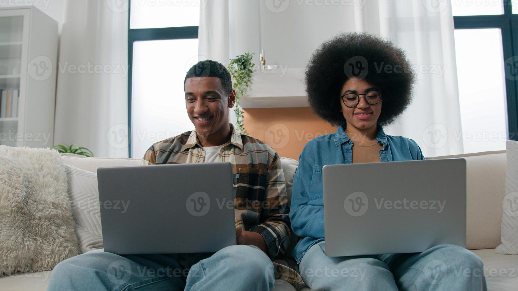 African American couple technology game addict family with two laptops playing online on couch home woman work with laptop man computer working freelancers with computers on sofa separate ignore photo