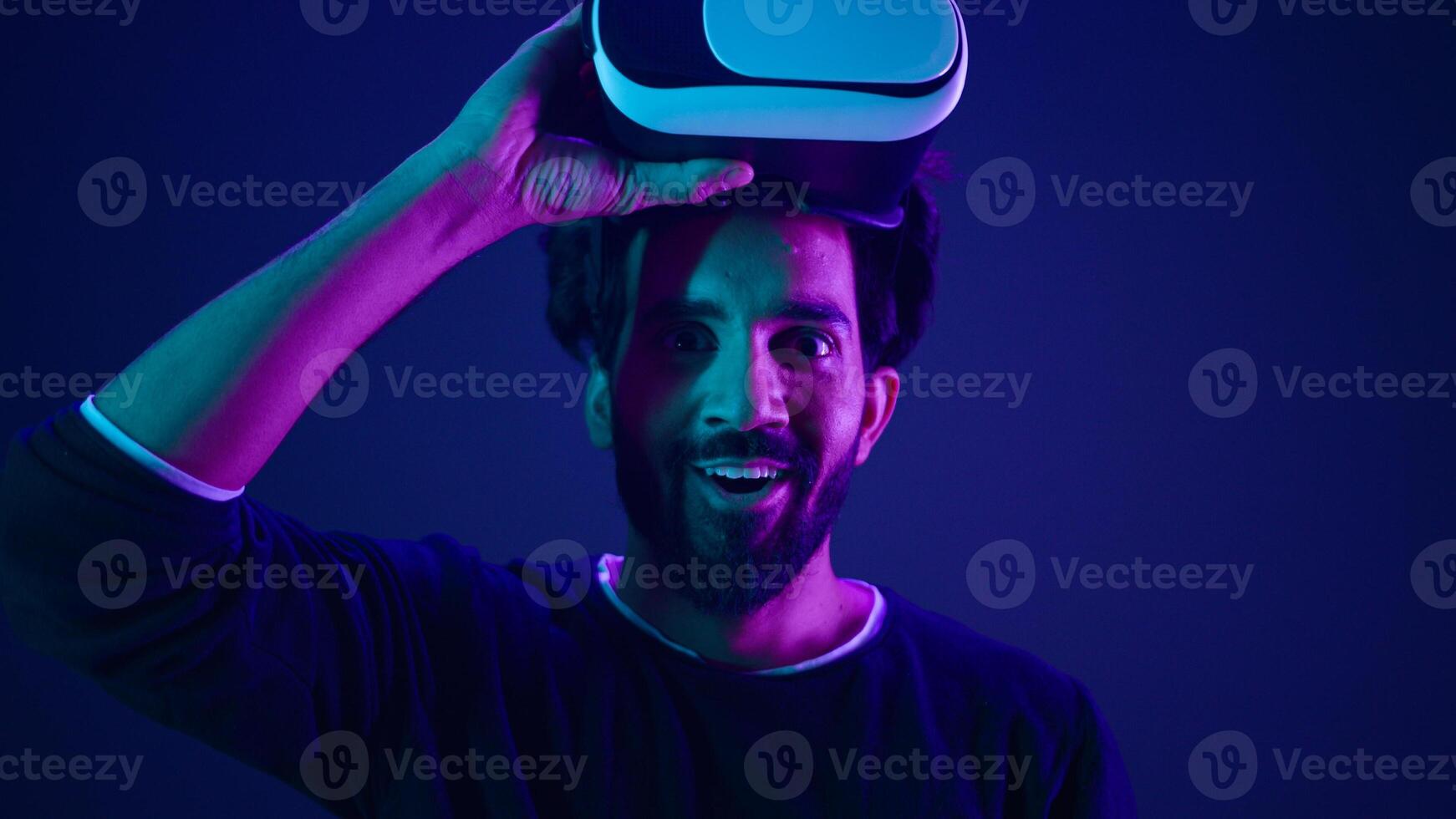Arabian man take off VR glasses excited smile amazed with metaverse virtual reality cyberspace Indian guy with 3d goggles helmet happy wow reaction after play game meta universe neon ultraviolet space photo