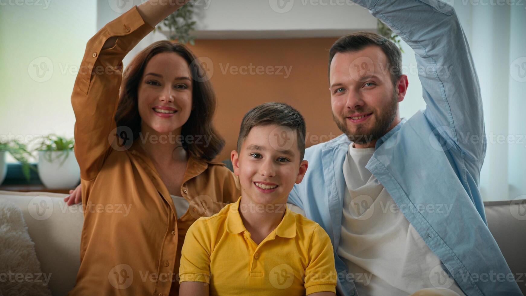 Happy smiling Caucasian family homeowners mother father son parents kid boy child sitting on couch in cozy living room make roof with hands dwelling symbol looking at camera new rented house bank loan photo