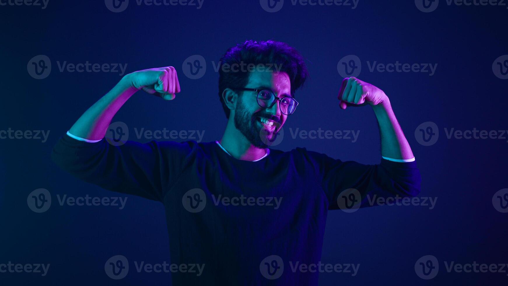 Funny Indian man slim guy fooling around show hands muscle biceps sport strong power bodybuilder ultraviolet neon studio background proud champion boast efficient security coding achievement level up photo