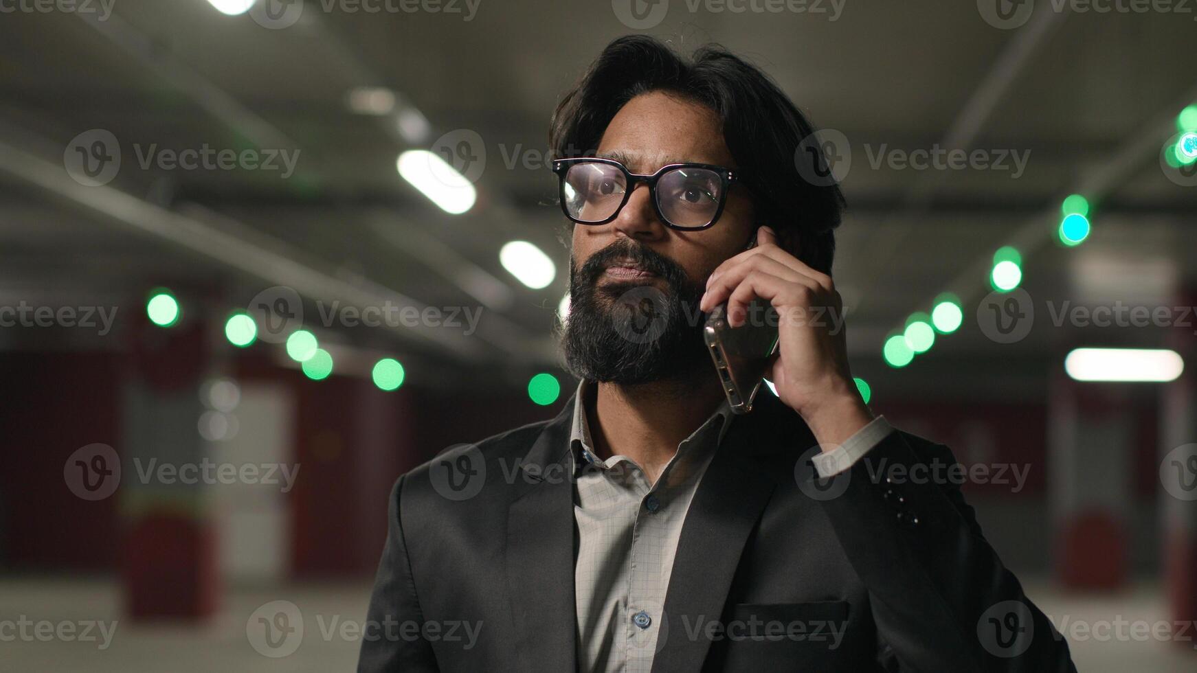 Emotional Indian man male businessman entrepreneur talking on mobile phone in underground parking answer business call using smartphone calling taxi guy employee speak talk communicate on telephone photo
