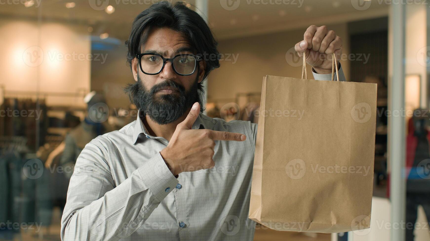Serious confident Indian man male guy businessman client customer buyer in clothing store shopping indoors showing paper bag pointing to package promote advertise boutique great purchase sale discount photo