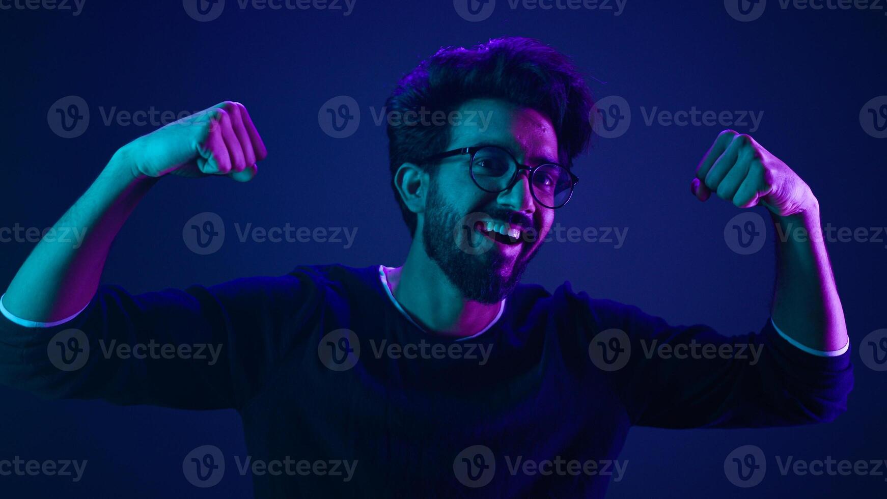 Funny Indian man slim guy fooling around show hands muscle biceps sport strong power bodybuilder ultraviolet neon studio background proud champion boast efficient security coding achievement level up photo