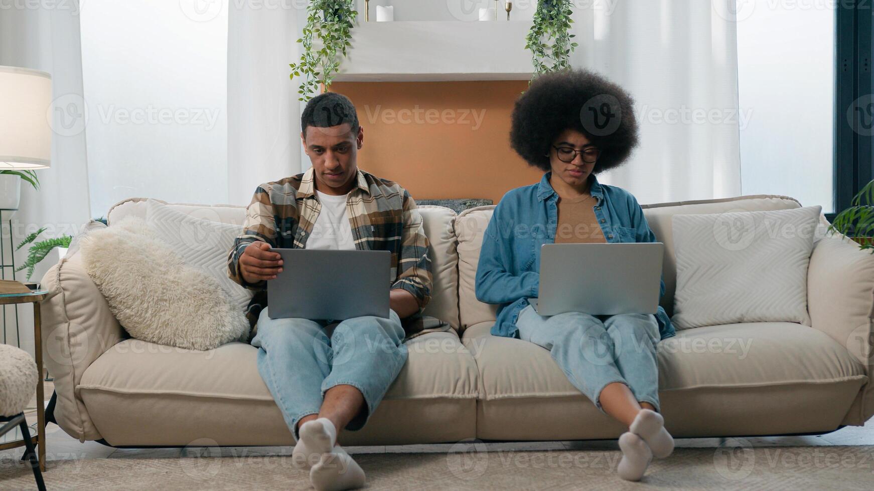 African American couple technology game addict family with two laptops playing online on couch home woman work with laptop man computer working freelancers with computers on sofa separate ignore photo