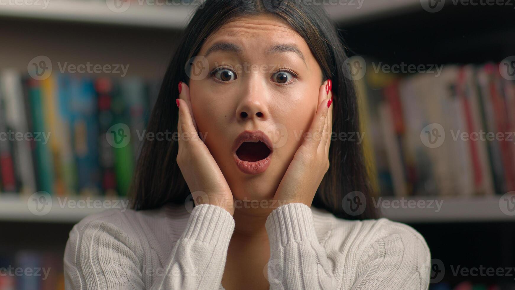 Close-up surprised young asian woman in shock with frightened expression opens mouth shocked by bad news feeling stress female student teacher standing in library near bookshelf worries about problem photo