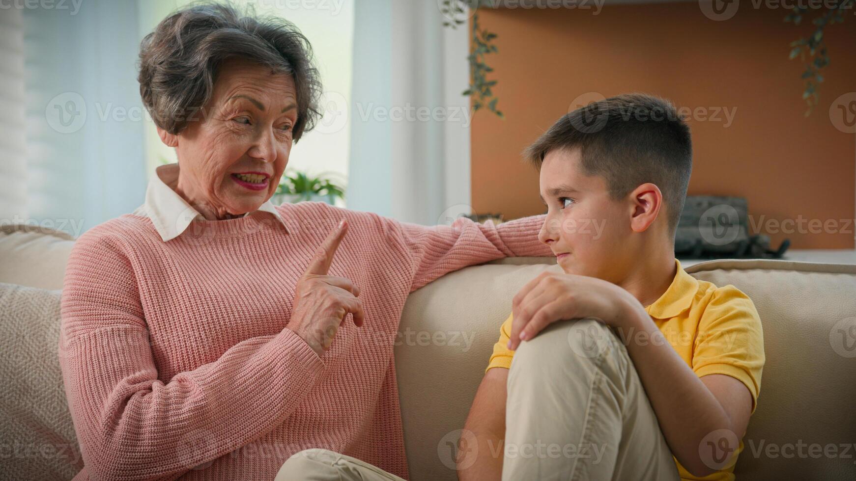 Caucasian grandmother explaining punishing spoiled grandson strict shaking index finger elderly caring woman grandma explain teaching discipline grandchild child kid boy on couch at home happy family photo