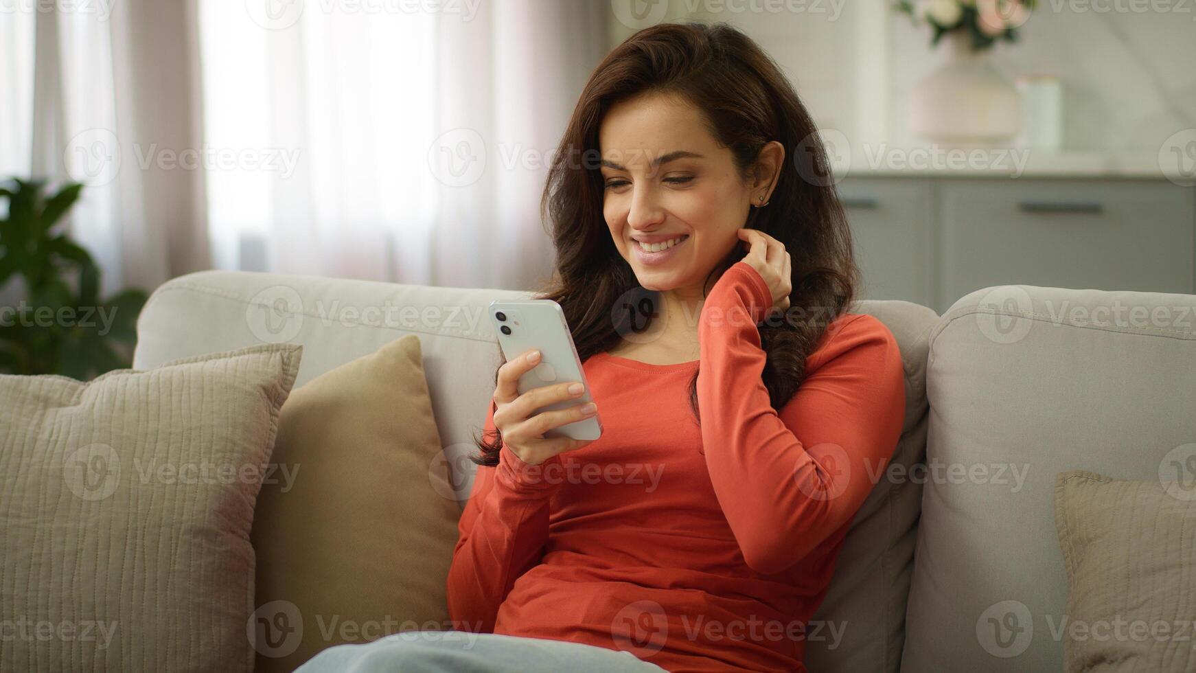 Happy joyful glad Caucasian woman female playful girl buyer owner at home apartment couch sofa hold mobile phone chatting using online dating app watch scrolling social media browsing internet photo