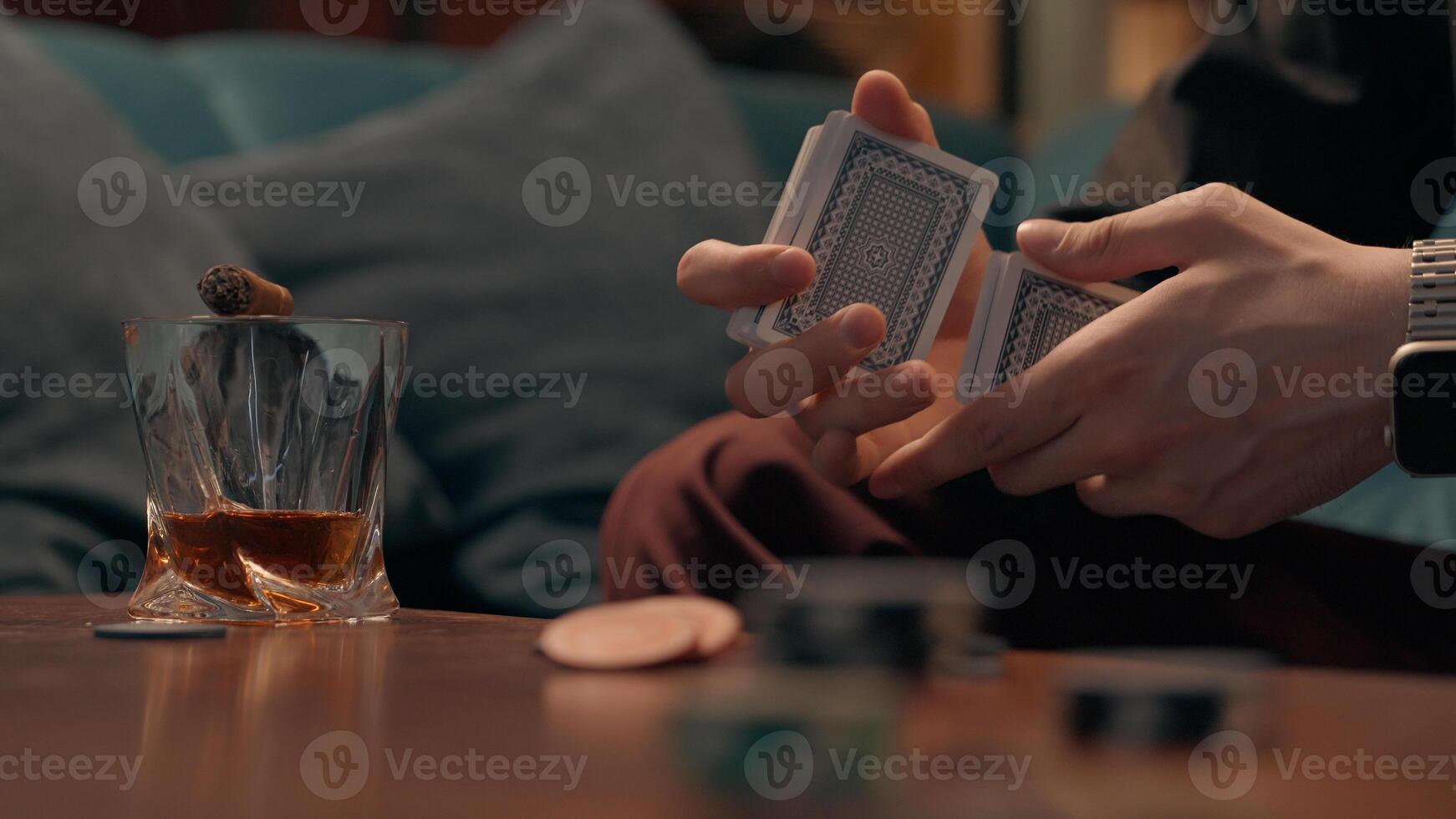 Unknown unrecognizable Caucasian guy man gambler poker player gamer dealer mixing playing cards blackjack game shuffling card drink alcohol whiskey smoking cigar gambling addiction bad habits at home photo