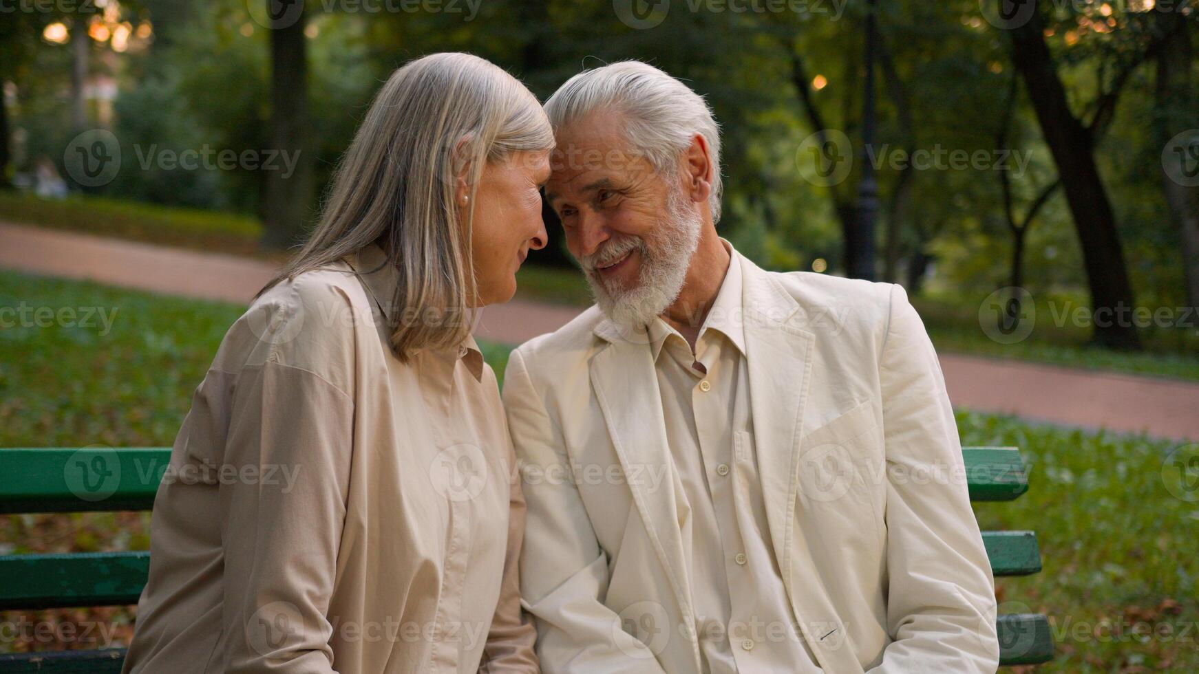Portrait cute romantic happy senior family smiling Caucasian elderly couple man woman cuddling talk discuss looking at camera resting relaxing together outside city park healthcare retirement marriage photo