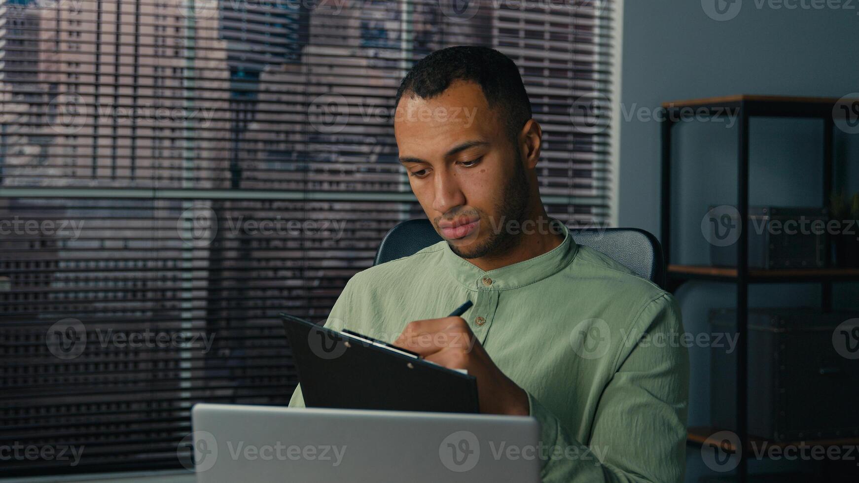African american man manager looking at laptop screen writing financial report analyzing data from internet young ethnic businessman write notes doing paperwork in office workplace making presentation photo