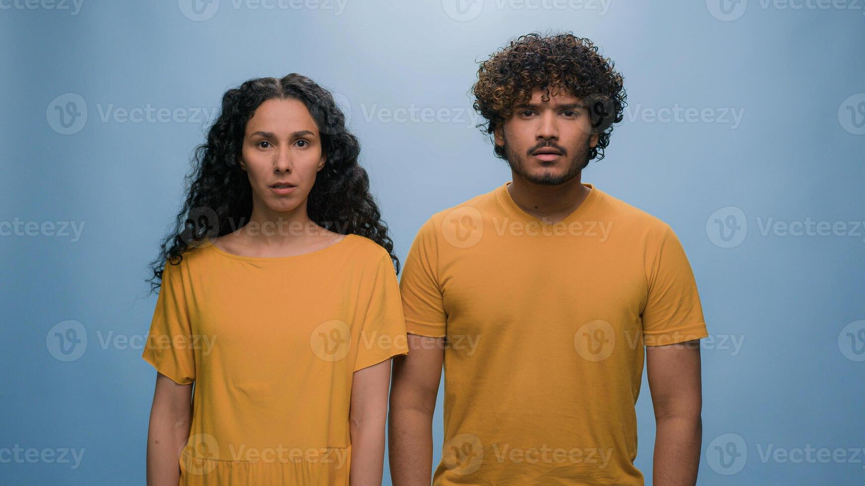 Multiracial diverse couple Hispanic woman Indian Arabian man wonder amazed shocked scared afraid frightened astonishment scare terrible horror reaction bad news crash disaster blue studio background photo