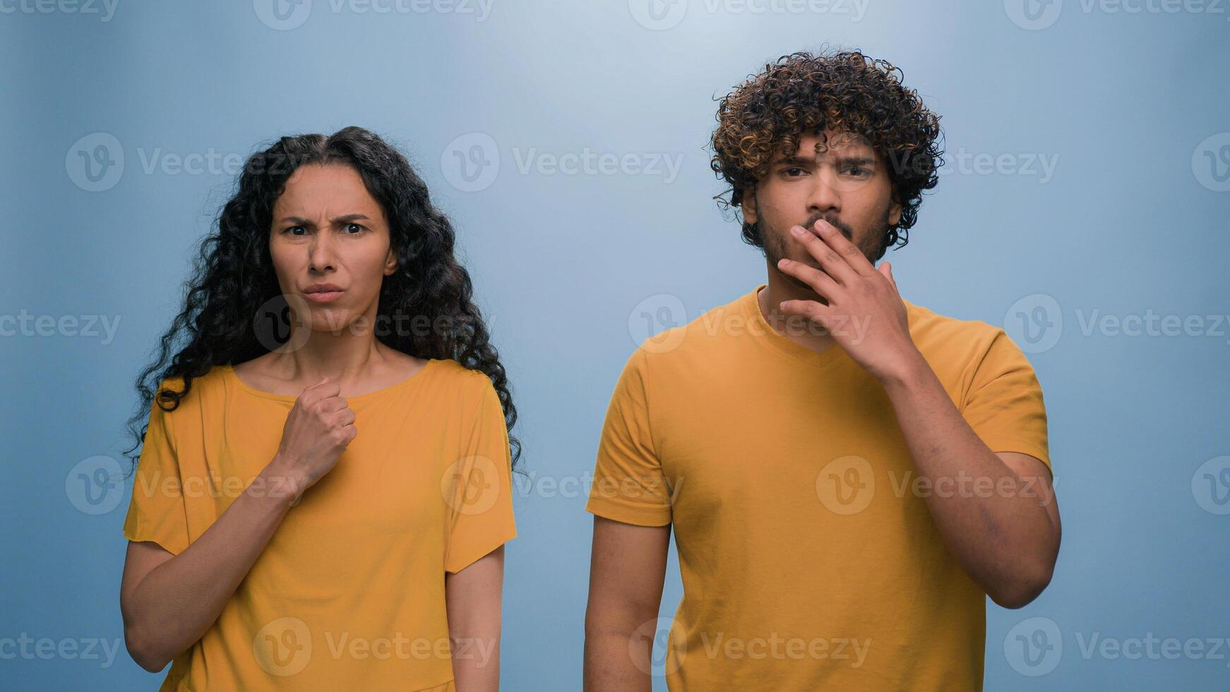 Multiracial shocked scared afraid couple amazed shocked Hispanic woman hiding behind Indian man astonishment wonder scare terrible horror ugly reaction blue studio background shock astonish fright photo